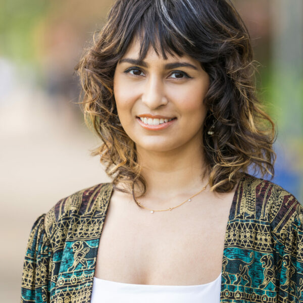 Photo of Sakshi Taneja, wearing a patterned printed cardigan, smiling at the camera.