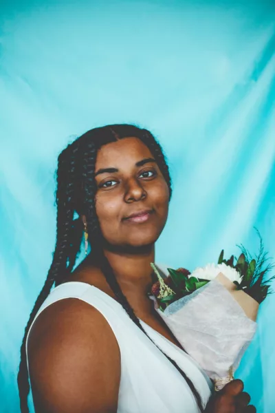 Photo of Alisha Lettman against a teal backdrop holding a bouquet of flowers and smiling at the camera.